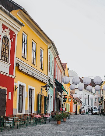 A street in Szentendre, Hungary, lined with colorful buildings and outdoor seating, adorned with hanging white lanterns.