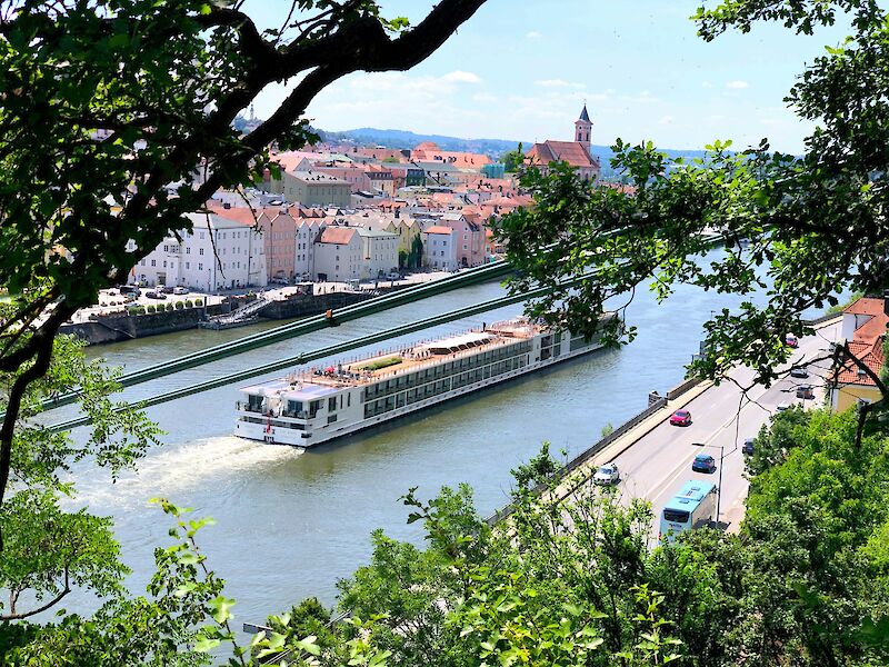 A barge cruising downriver, seen through foliage. Passau, Germany. Andi Steiner@Unsplash