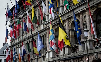 A historic building in Antwerp, Belgium, with multiple international flags hanging from flagpoles.