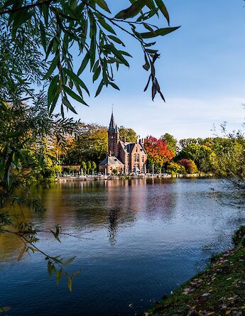 A castle-like building by a lake surrounded by autumn-colored trees in Bruges, Belgium.