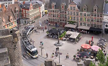 A view of a bustling square in Ghent, Belgium, with historical buildings, a tram, and people enjoying outdoor cafes.