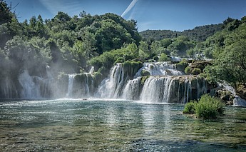 A cascading waterfall in Krka National Park, Croatia, surrounded by lush greenery under a clear blue sky.