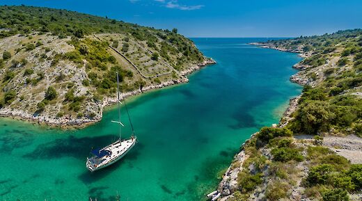 A sailboat in a turquoise bay surrounded by lush green hills in Trogir, Croatia.