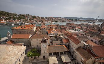 An aerial view of Trogir, Croatia, showcasing historic buildings with red roofs and a clock tower, near a body of water.