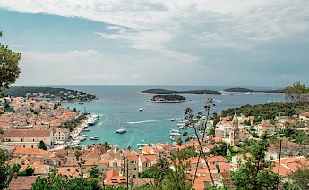 Panoramic view of Hvar Harbor, Croatia, showcasing red-roofed buildings, boats in turquoise waters, and small islands in the distance.