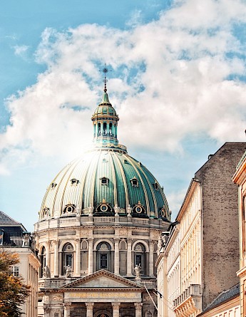 A grand architectural dome with intricate details rises against a partly cloudy sky in Copenhagen, Denmark.