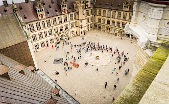 Aerial view of a courtyard at Kronborg Castle in Helsingør, Denmark, with groups of people scattered around the open space.