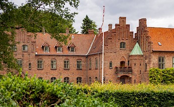 A historic brick building with a Danish flag is surrounded by greenery in Roskilde, Denmark.