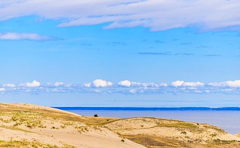 Sand dunes with sparse vegetation at the Curonian Spit, stretching towards a calm sea under a blue sky.