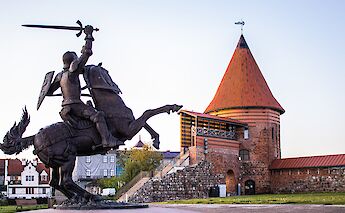 A statue of a knight on horseback in front of a historic brick tower structure in Kaunas, Lithuania.