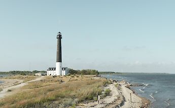 A lighthouse stands on a grassy shoreline overlooking the sea, situated on Saaremaa Island in Estonia.
