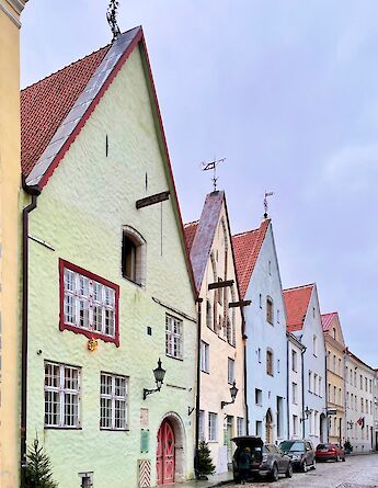 A row of colorful historic buildings with steep gabled roofs lining a cobblestone street in Tallinn, Estonia.