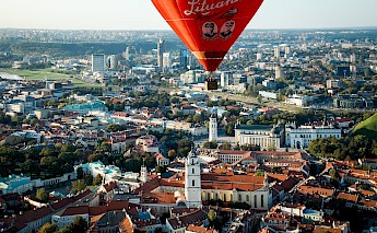 Aerial view of Vilnius, Lithuania, with a red hot air balloon in the foreground and the cityscape below.