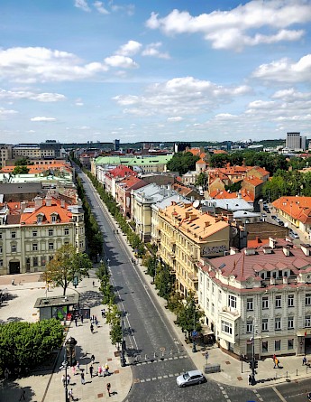 Aerial view of a wide street bordered by historic buildings and modern structures in Vilnius, Lithuania, under a partly cloudy sky.