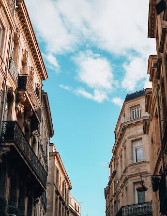 Stone buildings with ornate balconies against a blue sky in Bordeaux, France.