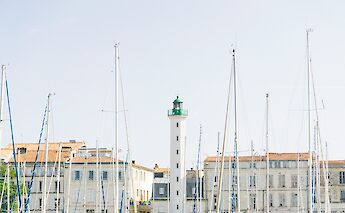 Sailboat masts in front of a lighthouse and historic buildings in La Rochelle, France.