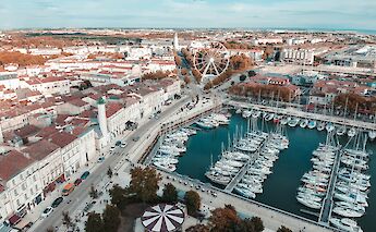 Aerial view of a marina in La Rochelle, France, showing boats docked alongside historic buildings and a ferris wheel.