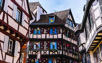 A colorful building in Colmar, France, adorned with flower decorations and traditional timber framing.