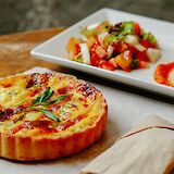 A French quiche garnished with herbs, served on a wooden table alongside a fresh salad on a white plate.