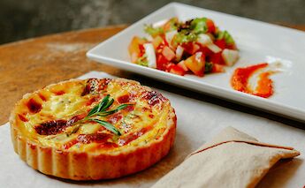A French quiche garnished with herbs, served on a wooden table alongside a fresh salad on a white plate.