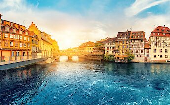 A sunset view of Strasbourg, France, featuring traditional half-timbered buildings along the river.