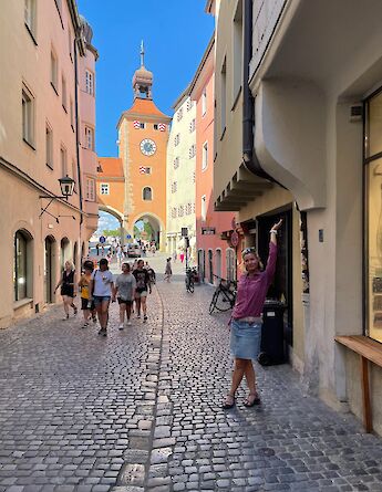 People walking through a cobblestone alleyway lined with historic buildings in Regensburg, Germany.