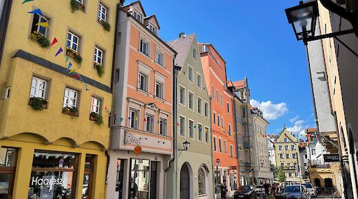 A street in Regensburg, Germany, lined with colorful historic buildings under a clear blue sky.