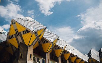 Distinctive yellow-and-grey cube houses under a partly cloudy sky in Rotterdam.