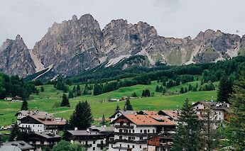 Traditional alpine village with rustic wooden buildings set against a backdrop of rugged mountains and green hills in the Dolomites.