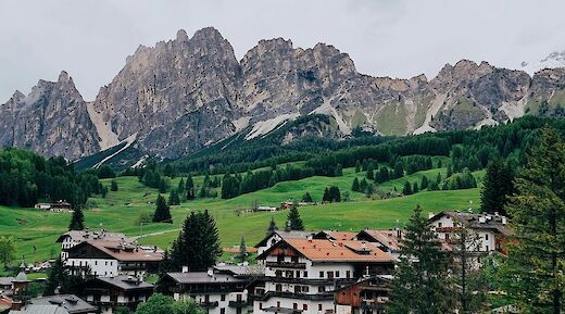 Traditional alpine village with rustic wooden buildings set against a backdrop of rugged mountains and green hills in the Dolomites.