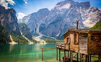 A wooden cabin on the shore of a clear mountain lake surrounded by the Dolomite mountains in South Tyrol, Italy.