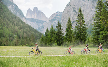 Cyclists enjoying a ride through alpine meadows with towering peaks in the background, in the Dolomites.