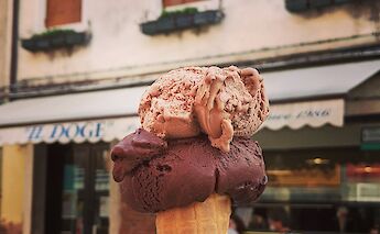 A cone of chocolate and hazelnut gelato held in front of a shop window in Italy.