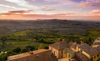 A scenic view of the Tuscan countryside with rolling hills and tiled rooftops at sunset.