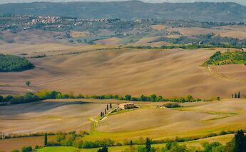 A landscape view of rolling hills and farmland in Tuscany, Italy, with a small village in the distance.