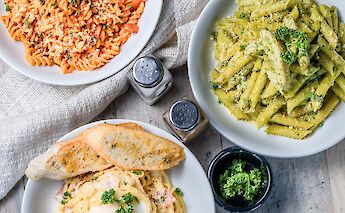 Three plates of pasta dishes garnished with herbs and cheese, accompanied by a salt and pepper shaker.