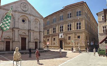 Piazza Pio II in Pienza, Tuscany, Italy, featuring a historic church and adjacent buildings with people walking in the square.
