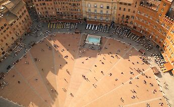 An aerial view of the Piazza del Campo in Siena, Italy, with groups of people scattered across its shell-shaped layout.