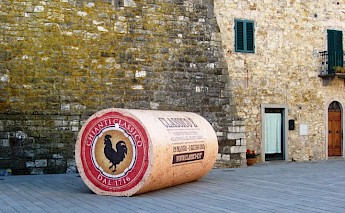 A large replica wine cork displayed against a stone building in a town square in Tuscany, Italy.