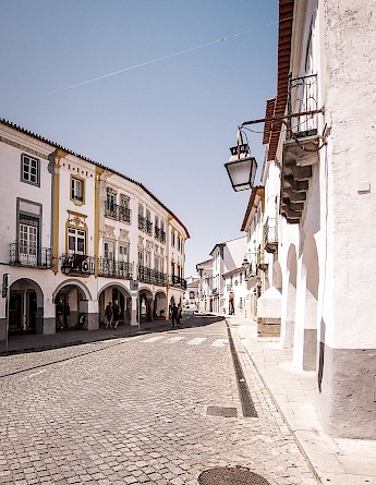 A street scene in Évora, Portugal, featuring ornate buildings with balconies and arches on a sunny day.