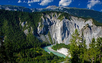 Panoramic view of a river winding through lush green forests and steep, rocky hills.
