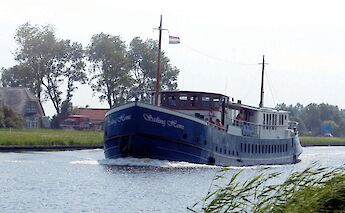 -The boat Sailing Home is cruising along a canal with trees in the background.