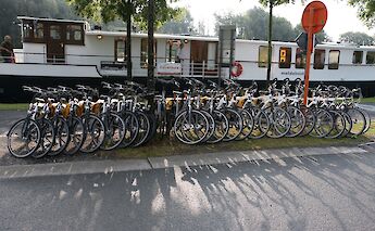 A line of bicycles is parked next to a boat.