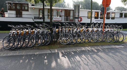 A line of bicycles is parked next to a boat.