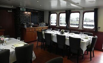 A dining area with elegantly set tables, chairs, and large windows providing a view outside.