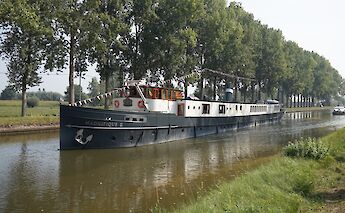 A boat named Magnifique II navigating a canal lined with trees.