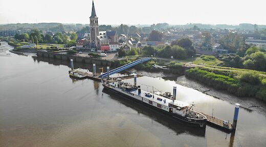 An aerial view of the Magnifique II docked by a small town with a prominent church and surrounding greenery.