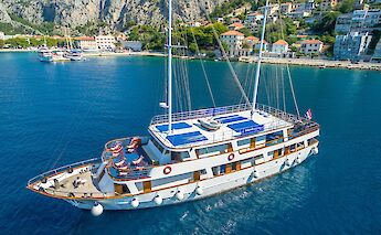 Aerial view of a white yacht with blue awnings named Romantica sailing near a coastal town with…