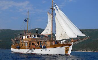 A traditional wooden sailboat named Panagiota with sails unfurled, sailing on the sea against a&hellip;