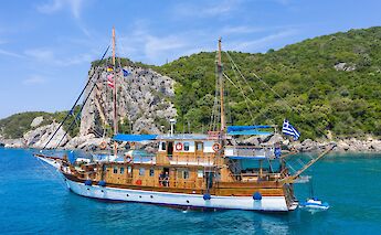 A wooden sailboat named Panagiota anchored near a rocky coastline, with clear blue water and green&hellip;